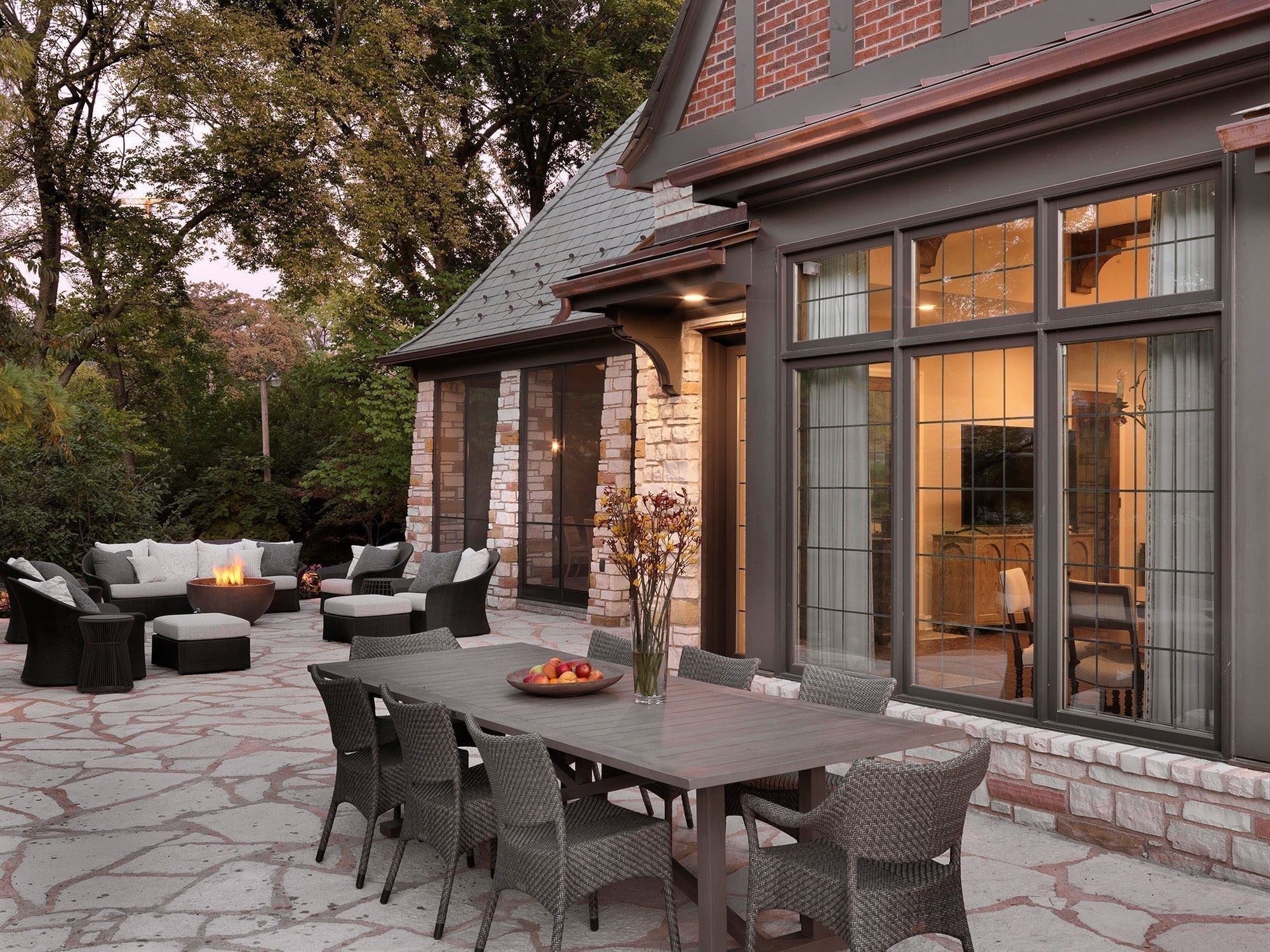 Outdoor patio at 1920s Clayton Estate with long stone table, white seating, dark accents, and fire feature at dusk — luxury design by Ättlingar.