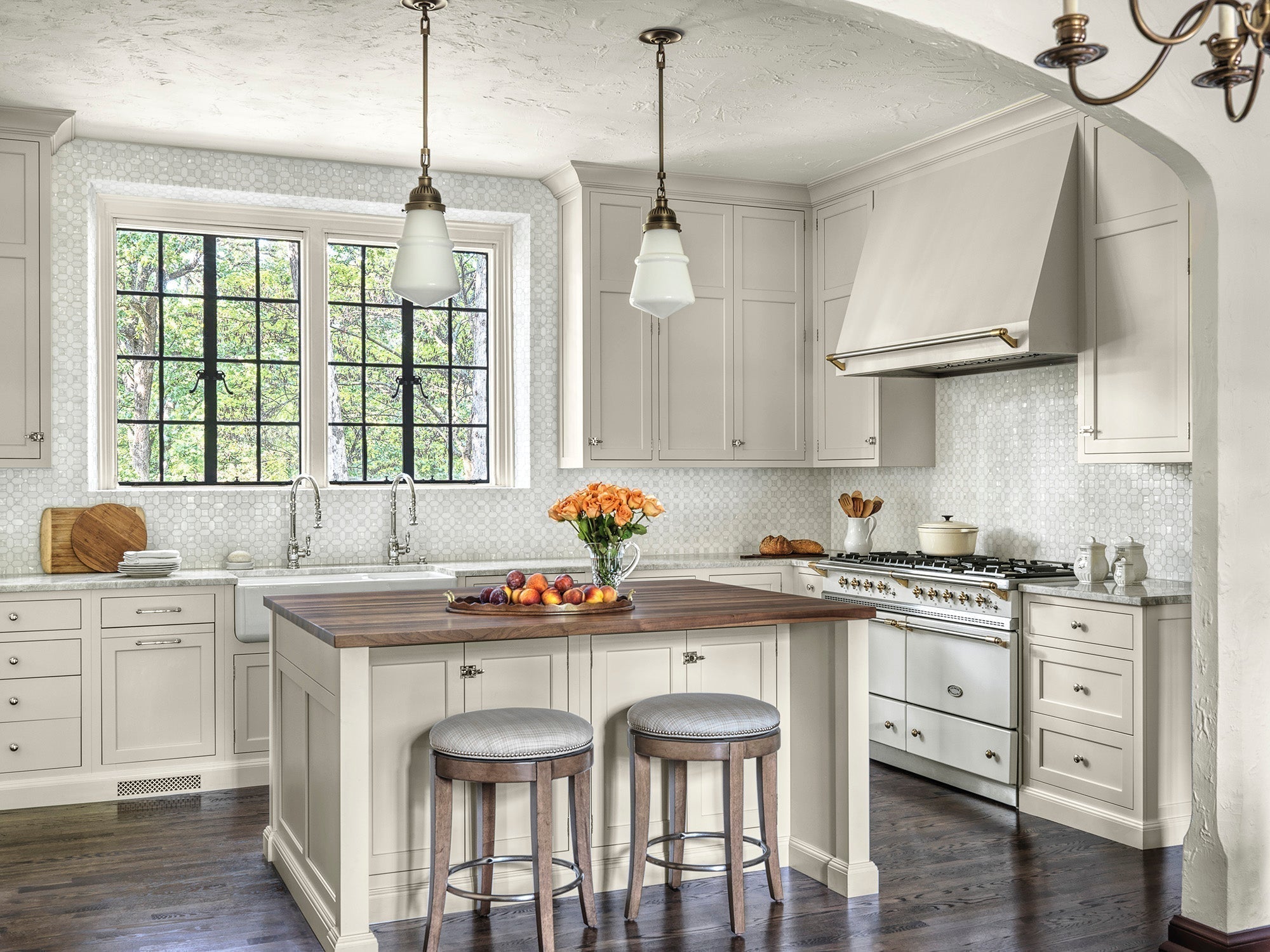 Elegant Ladue Tudor kitchen with arched entryway, black iron windows, cream cabinetry, and rustic wood accents designed by Ättlingar.